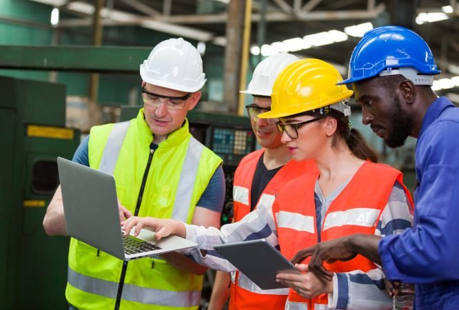 Diversity factory worker working with computer laptop in factory. Male and female worker wearing safety uniform, helmet and gloves at work factory. Group of worker working at factory